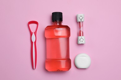 Photo of Tongue cleaner, dental floss, mouthwash and hourglass on pink background, flat lay