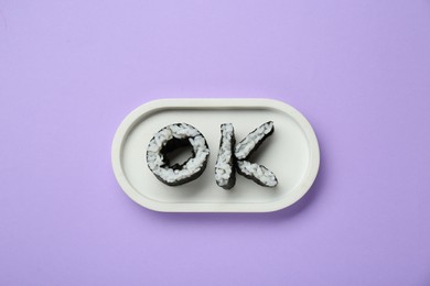 Photo of Word Ok made of sushi rolls on violet background, top view