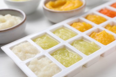 Photo of Different purees in ice cube tray and bowls on white table, closeup. Ready for freezing