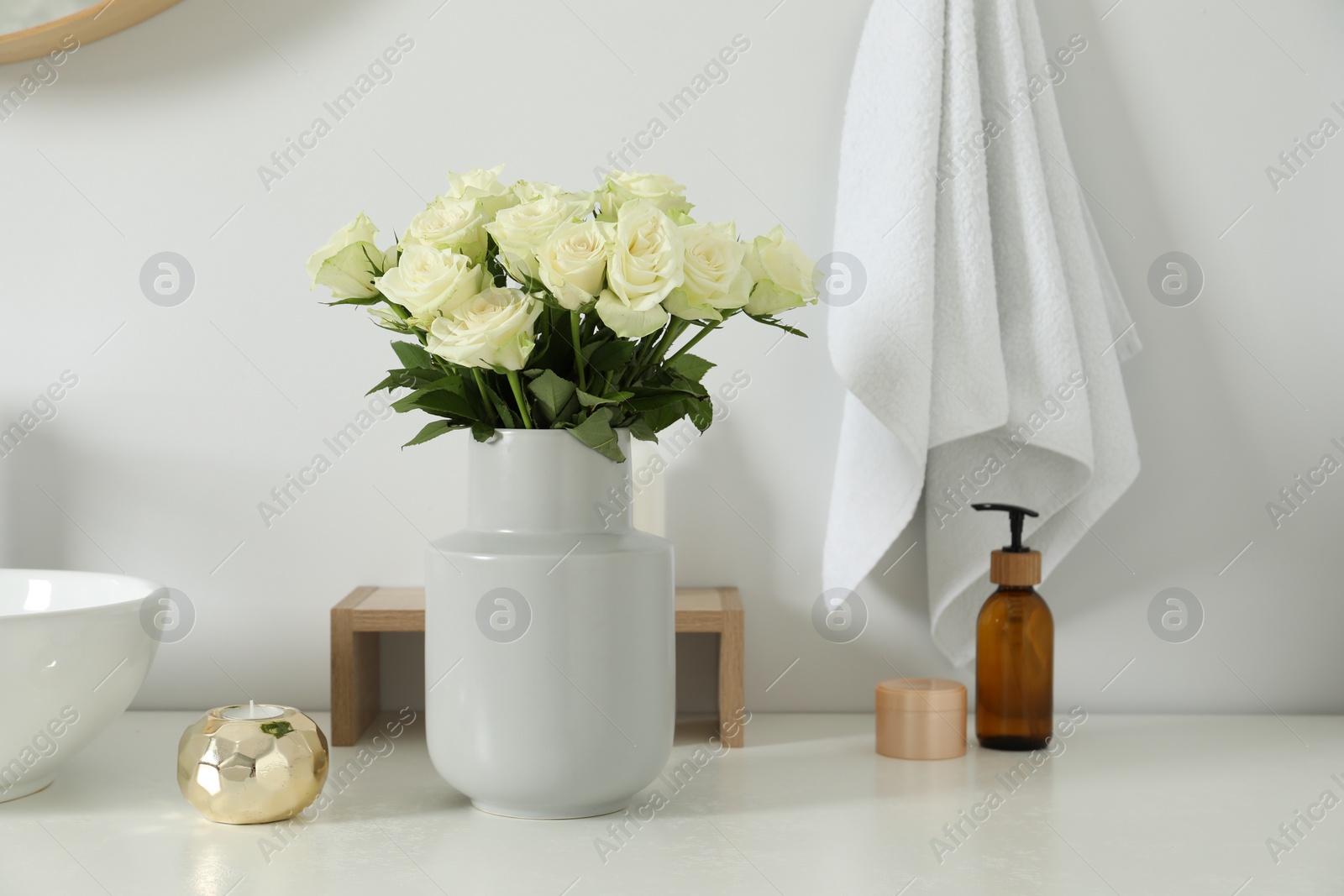 Photo of Vase with beautiful white roses and toiletries near sink in bathroom