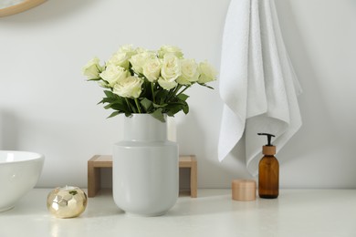 Vase with beautiful white roses and toiletries near sink in bathroom