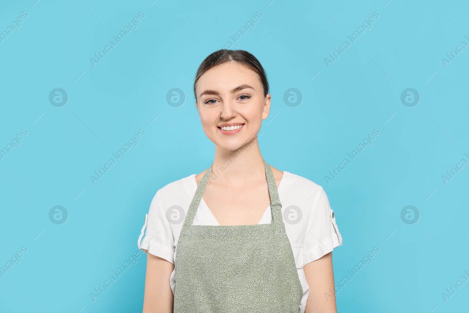 Photo of Beautiful young woman in clean apron with pattern on light blue background