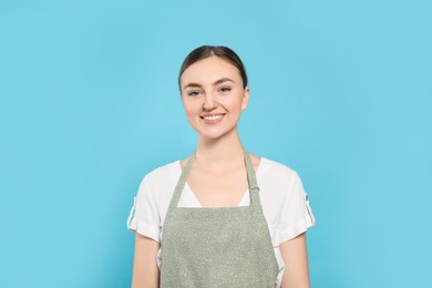 Beautiful young woman in clean apron with pattern on light blue background