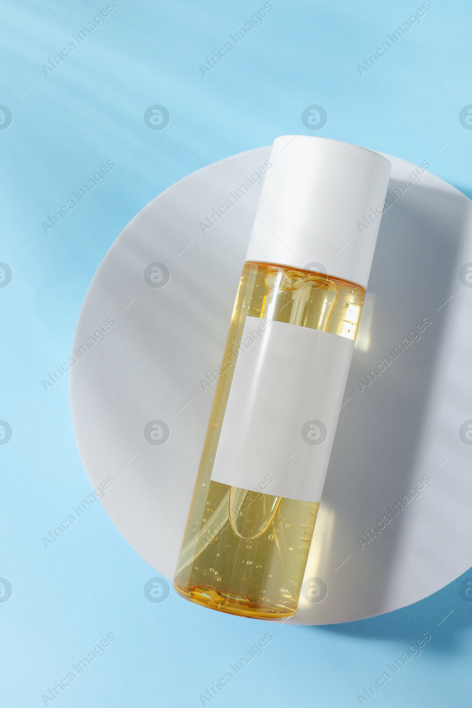 Photo of Bottle of cosmetic oil on light blue background, top view