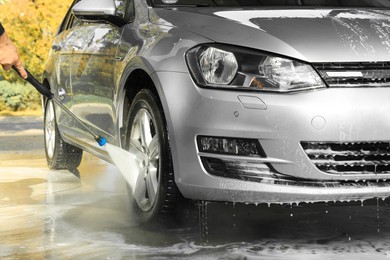 Photo of Man washing auto with high pressure water jet at outdoor car wash, closeup