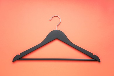 Photo of Empty black hanger on coral background, top view