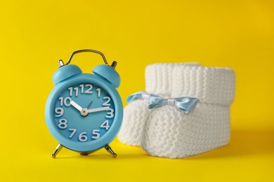 Photo of Alarm clock and baby booties on yellow background. Time to give birth