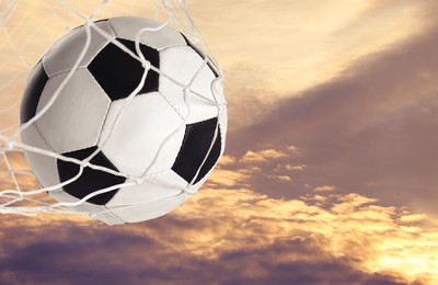 Image of Soccer ball in net against sky at sunset