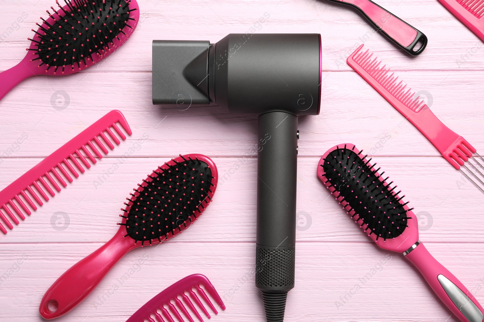Photo of Hair dryer and different brushes on pink wooden table, flat lay. Professional hairdresser tool
