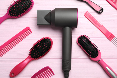 Hair dryer and different brushes on pink wooden table, flat lay. Professional hairdresser tool