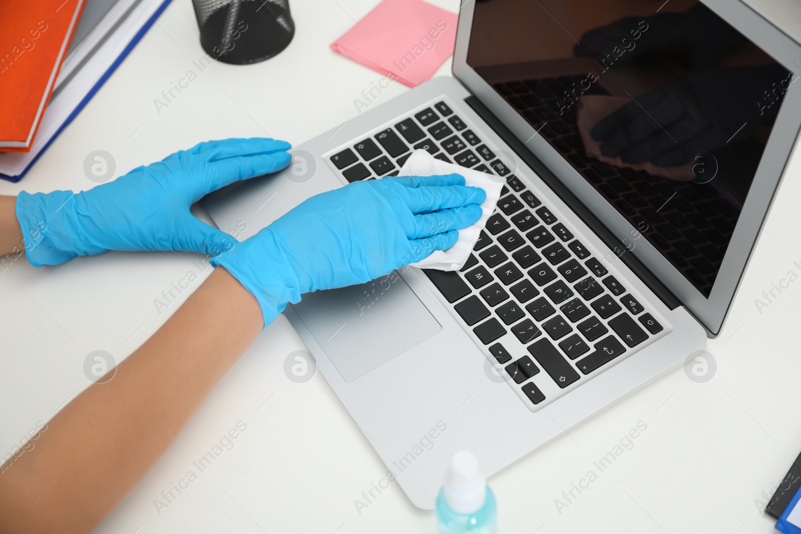 Photo of Woman cleaning laptop with antibacterial wipe at table in office, closeup