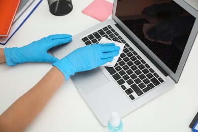 Photo of Woman cleaning laptop with antibacterial wipe at table in office, closeup