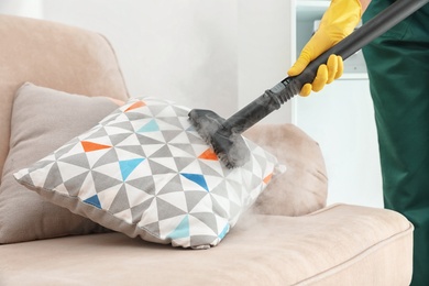 Janitor removing dirt from sofa cushion with steam cleaner, closeup