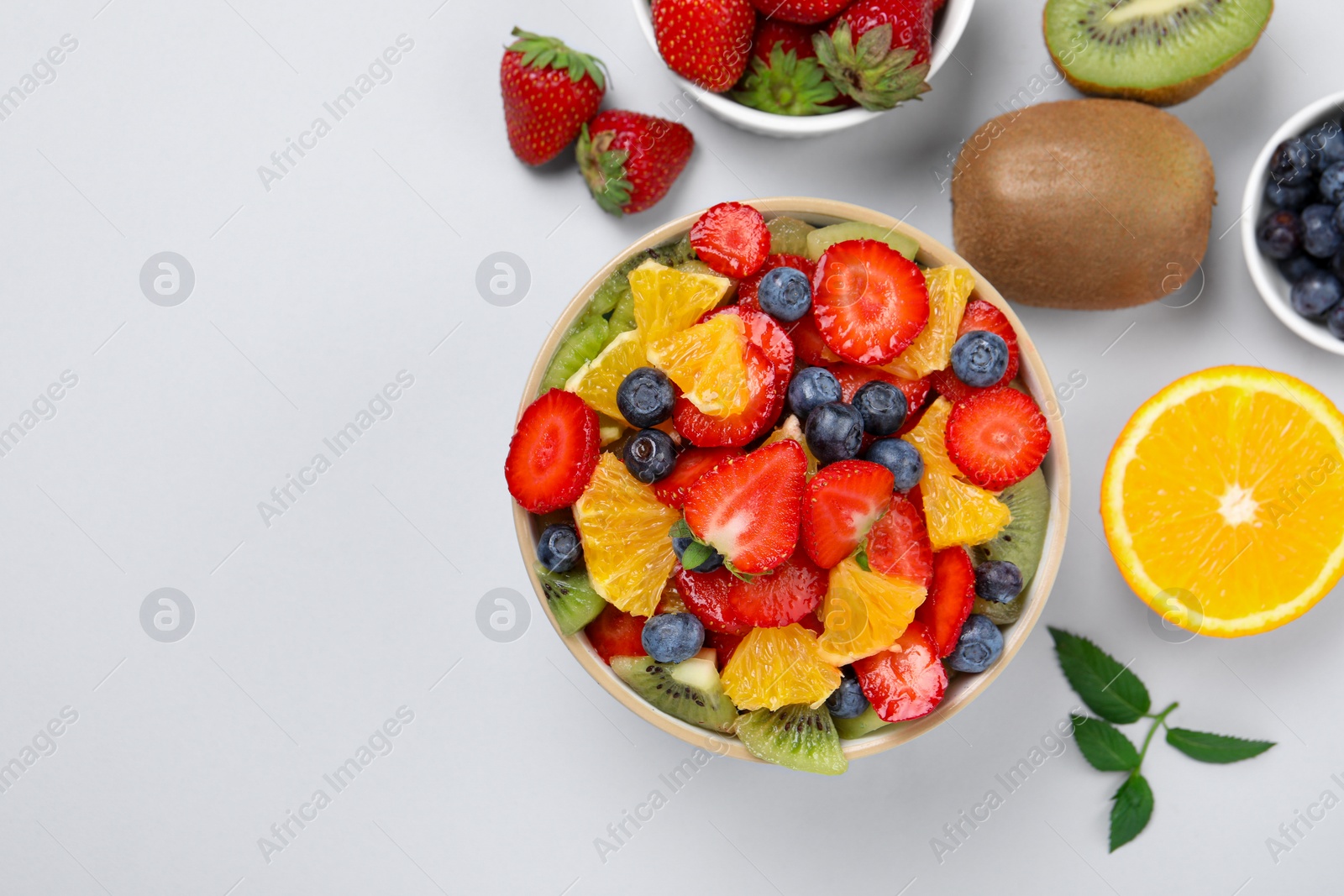 Photo of Yummy fruit salad in bowl and ingredients on light background, flat lay. Space for text