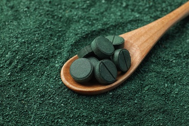 Photo of Spoon of spirulina pills on green algae powder