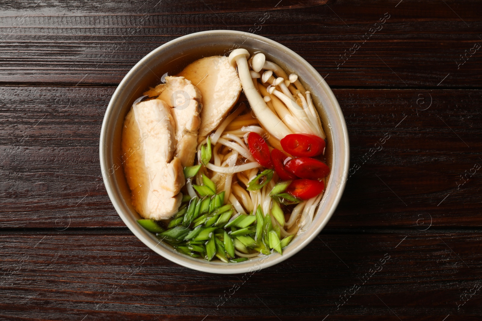 Photo of Delicious ramen with meat and mushrooms in bowl on wooden table, top view. Noodle soup