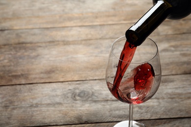 Pouring red wine from bottle into glass on wooden background. Space for text