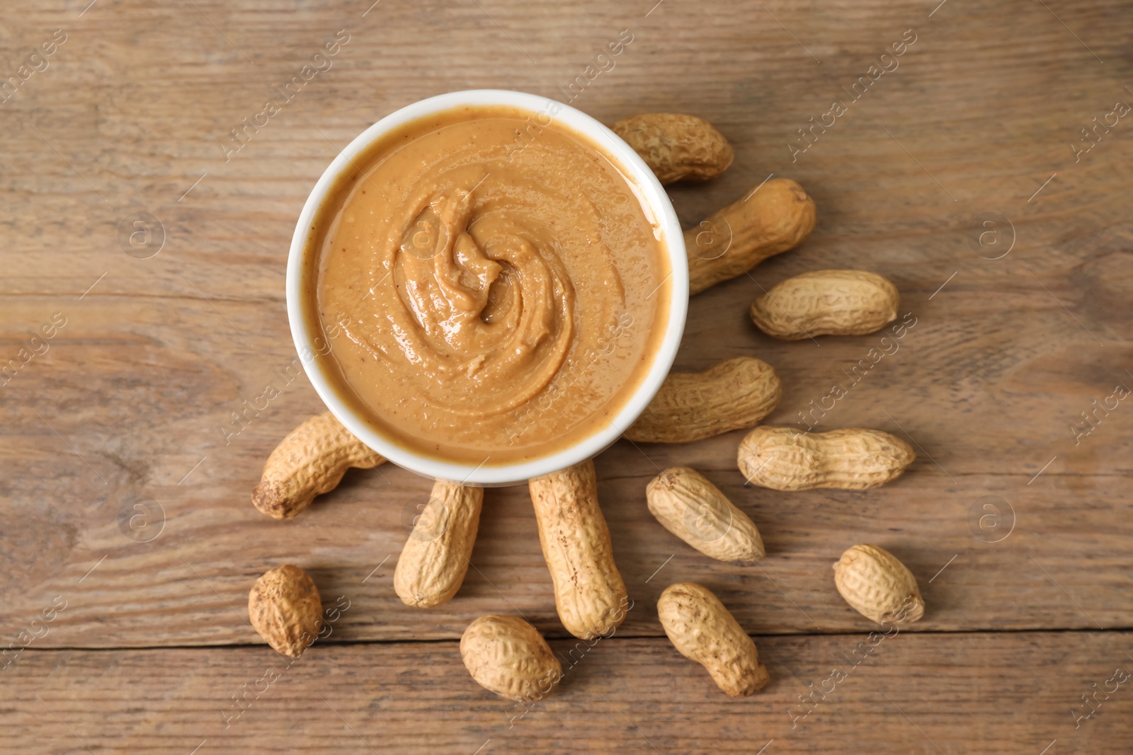 Photo of Delicious nut butter in bowl and peanuts on wooden table, top view