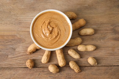 Photo of Delicious nut butter in bowl and peanuts on wooden table, top view