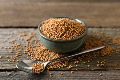 Bowl and spoon of mustard seeds on wooden table, closeup