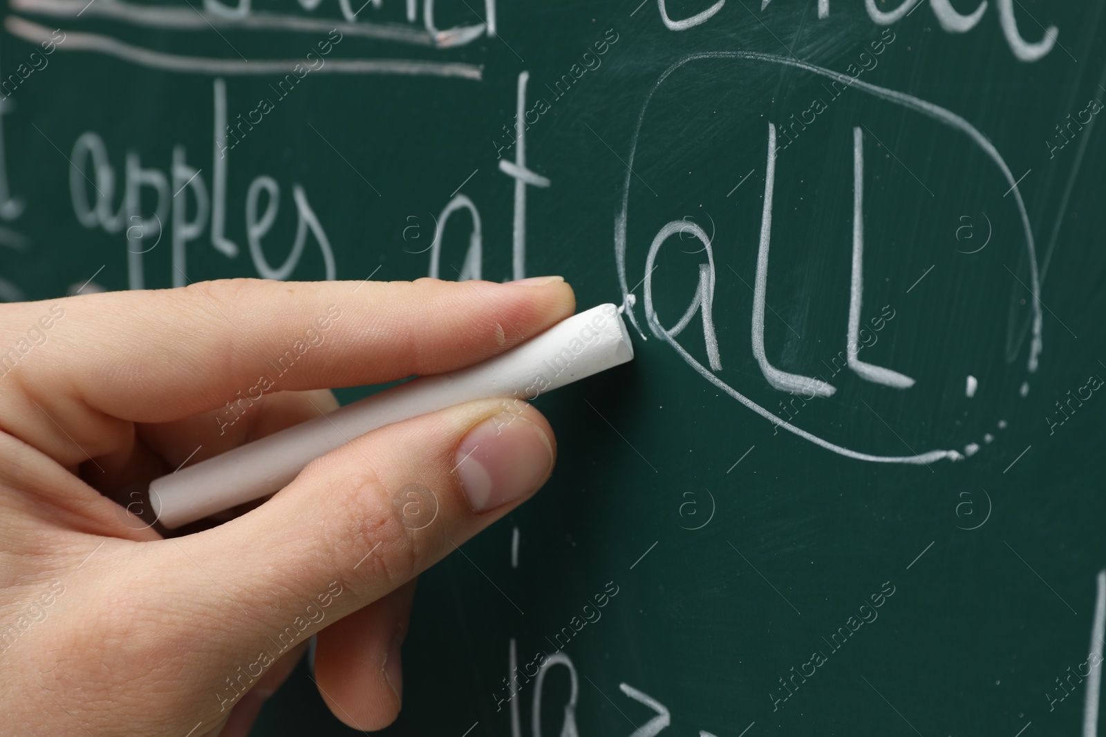 Photo of English teacher writing with chalk on green chalkboard, closeup