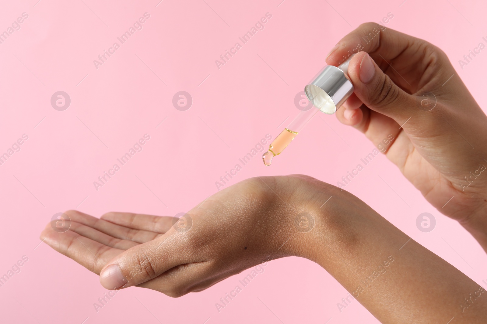 Photo of Woman applying cosmetic serum onto her hand on pink background, closeup