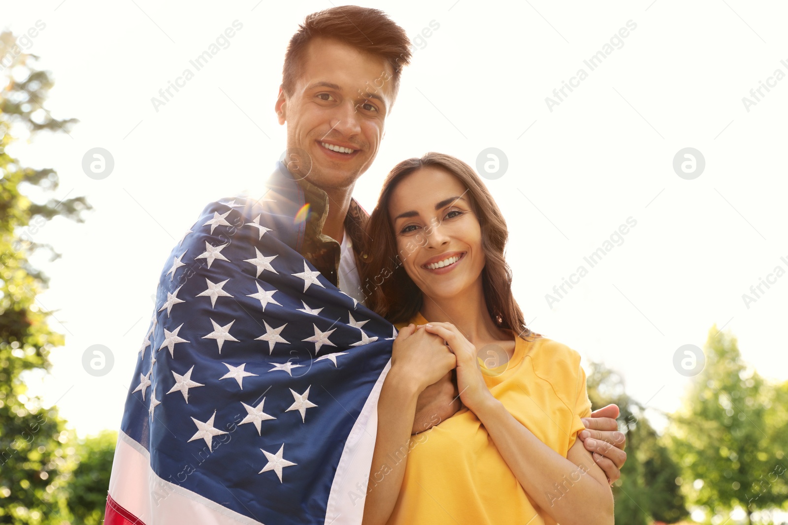 Photo of Man in military uniform with American flag and his wife at sunny park