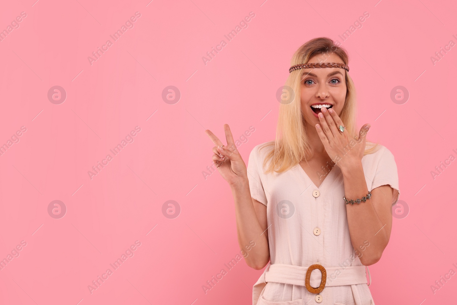 Photo of Portrait of hippie woman showing peace sign on pink background. Space for text