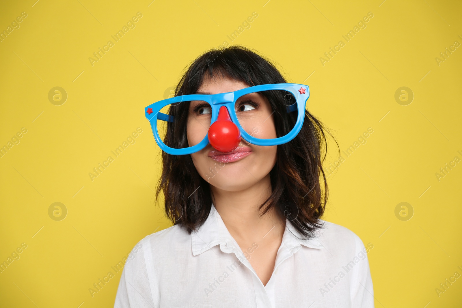 Photo of Joyful woman with funny glasses on yellow background. April fool's day