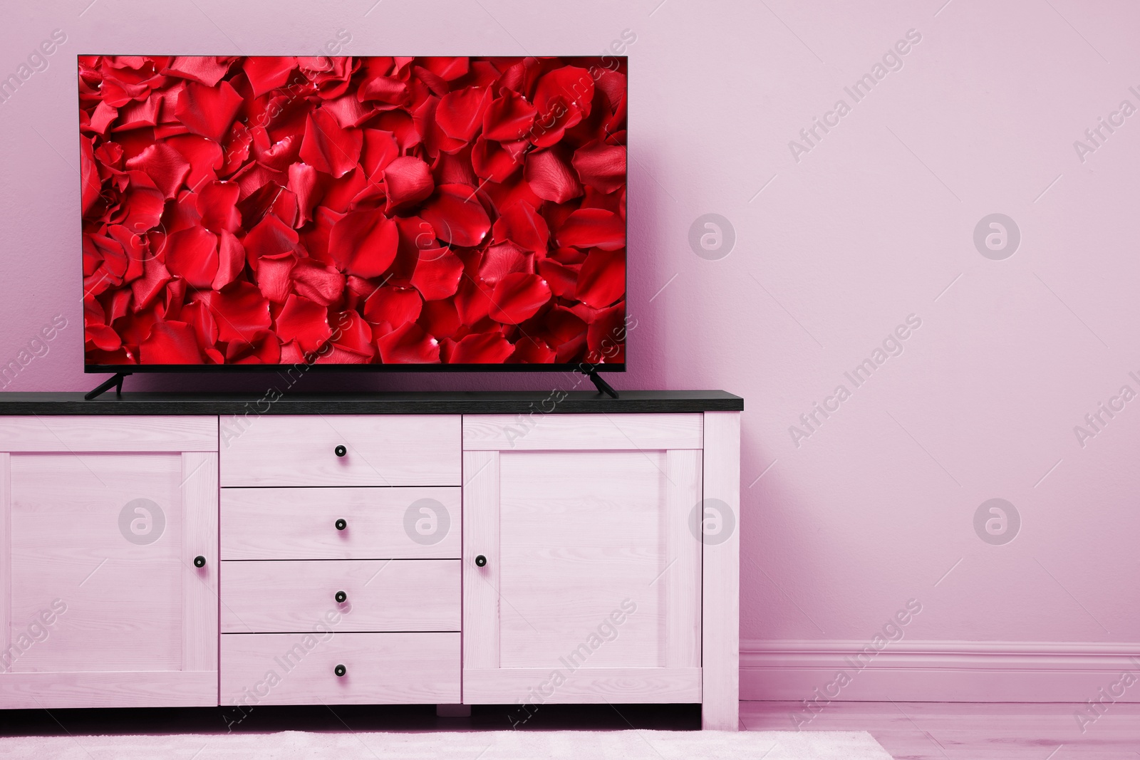 Image of TV screen with red rose petals on commode near pink wall in room, space for text