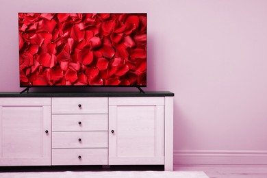 TV screen with red rose petals on commode near pink wall in room, space for text