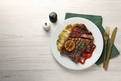 Photo of Delicious grilled beef steak and vegetables served on light wooden table, top view. Space for text