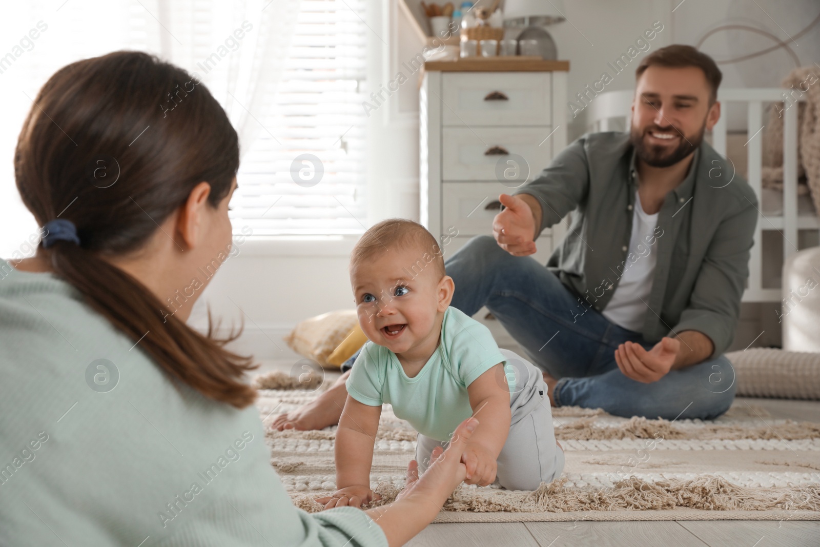 Photo of Happy parents helping their baby to crawl on floor at home