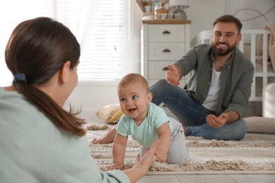 Photo of Happy parents helping their baby to crawl on floor at home