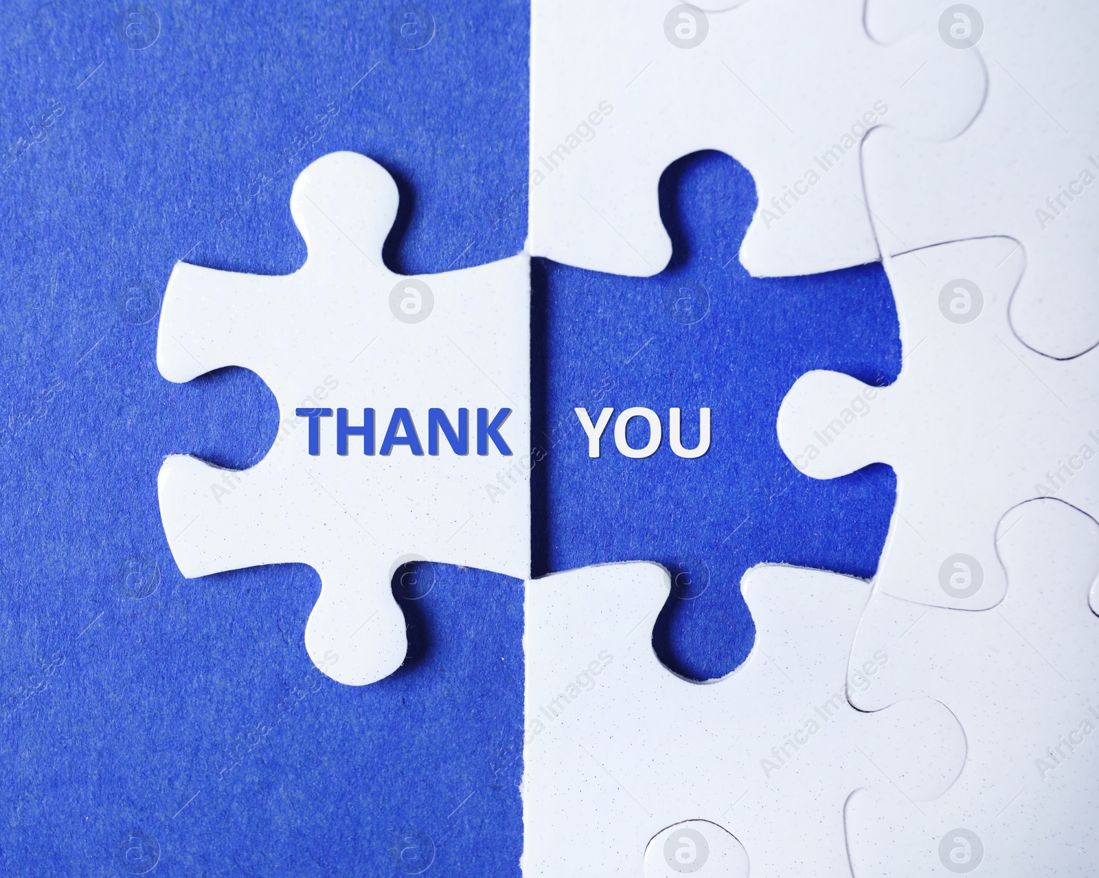 Image of White puzzle with separated piece and phrase THANK YOU on blue background, top view