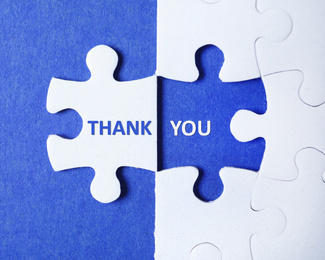 Image of White puzzle with separated piece and phrase THANK YOU on blue background, top view