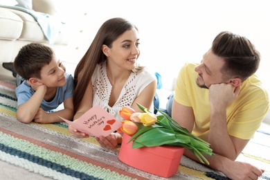 Happy woman reading handmade card near her husband and son at home. Mother's day celebration