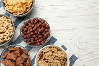 Different delicious breakfast cereals on white wooden table, top view. Space for text