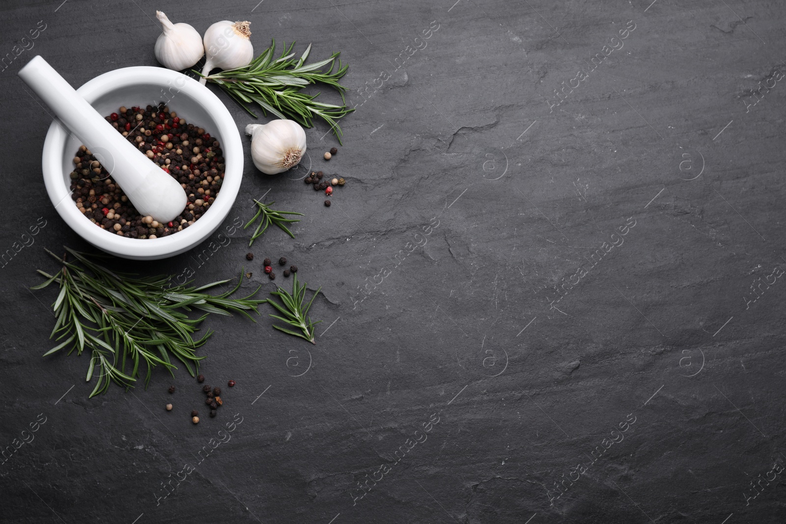 Photo of Sprigs of rosemary, mortar and garlic on black background, flat lay. Space for text