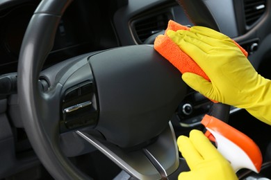 Photo of Woman cleaning steering wheel with rag in car, closeup