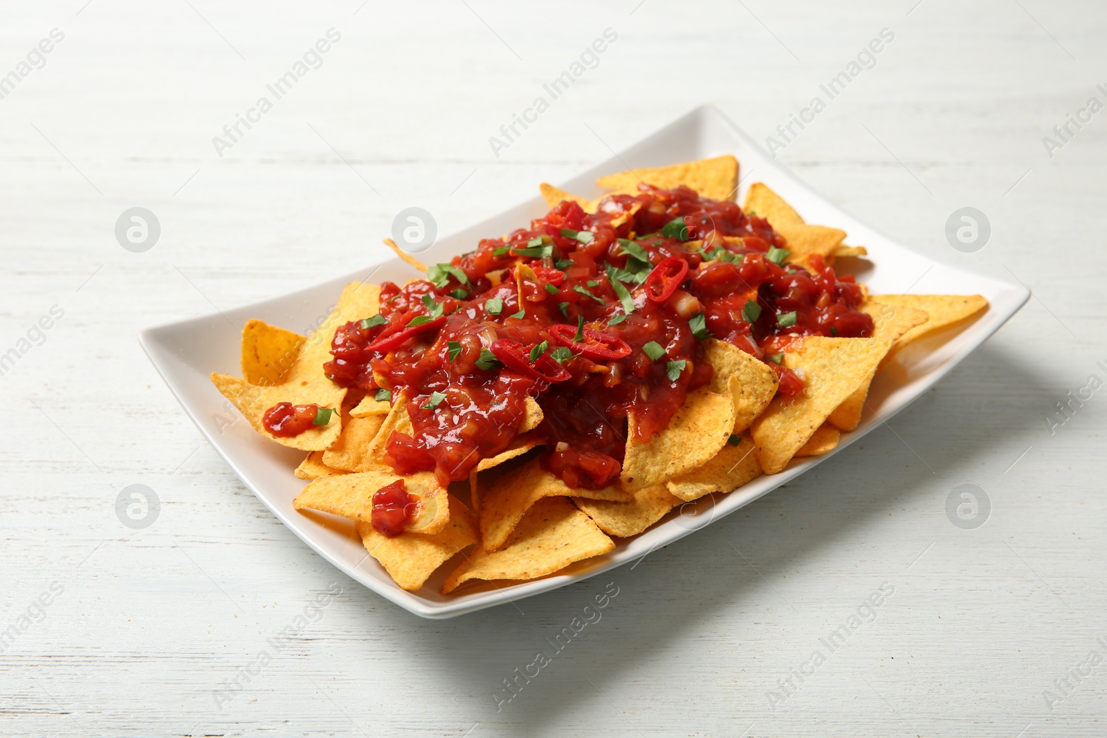 Photo of Plate of delicious mexican nachos chips with salsa sauce on white wooden table