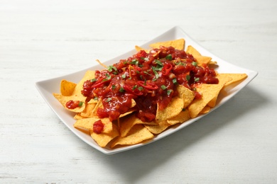 Photo of Plate of delicious mexican nachos chips with salsa sauce on white wooden table