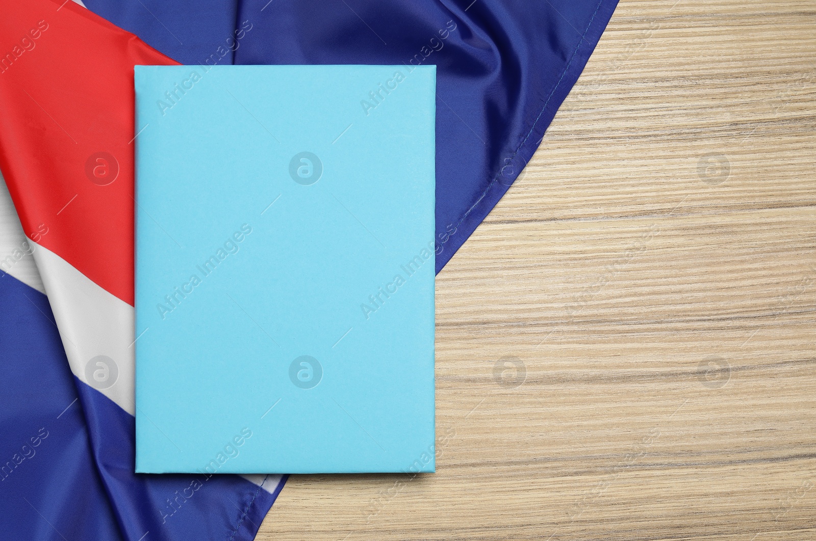 Photo of Learning foreign language. Book and flag of United Kingdom on wooden table, top view with space for text