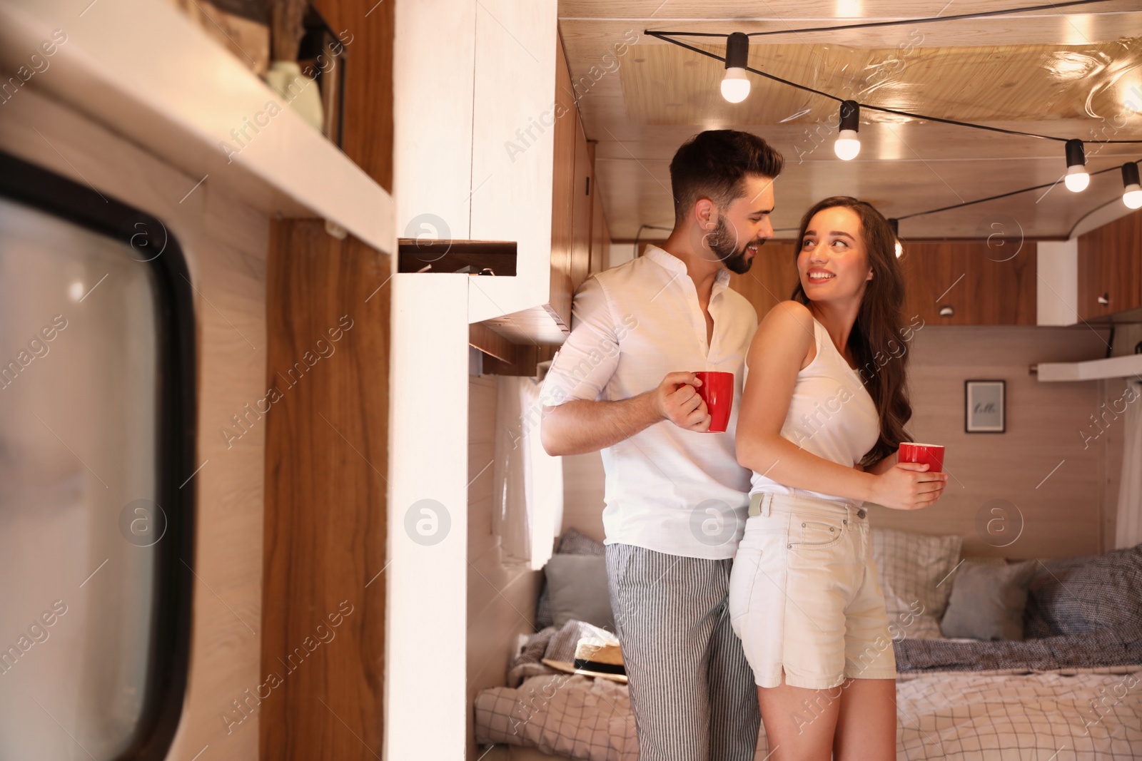 Photo of Happy young couple with cups in trailer. Camping vacation