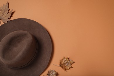 Stylish hat and autumn leaves on orange background, flat lay. Space for text