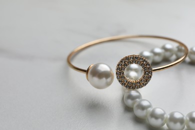 Photo of Elegant bracelets with pearls on white marble table, closeup