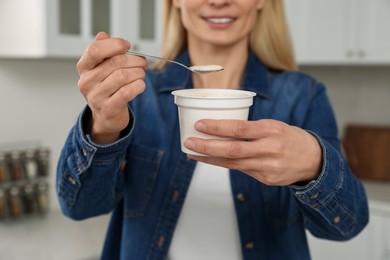 Photo of Woman holding plastic cup and spoon with tasty yogurt in kitchen, closeup