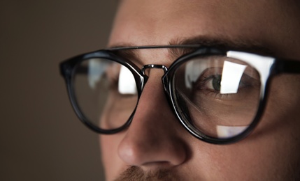 Photo of Young man wearing glasses on color background, closeup. Ophthalmology service