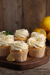 Delicious cupcakes with white cream and lemon zest on wooden table, closeup