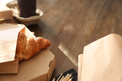 Paper bag with pastry and takeaway food on wooden table. Space for text